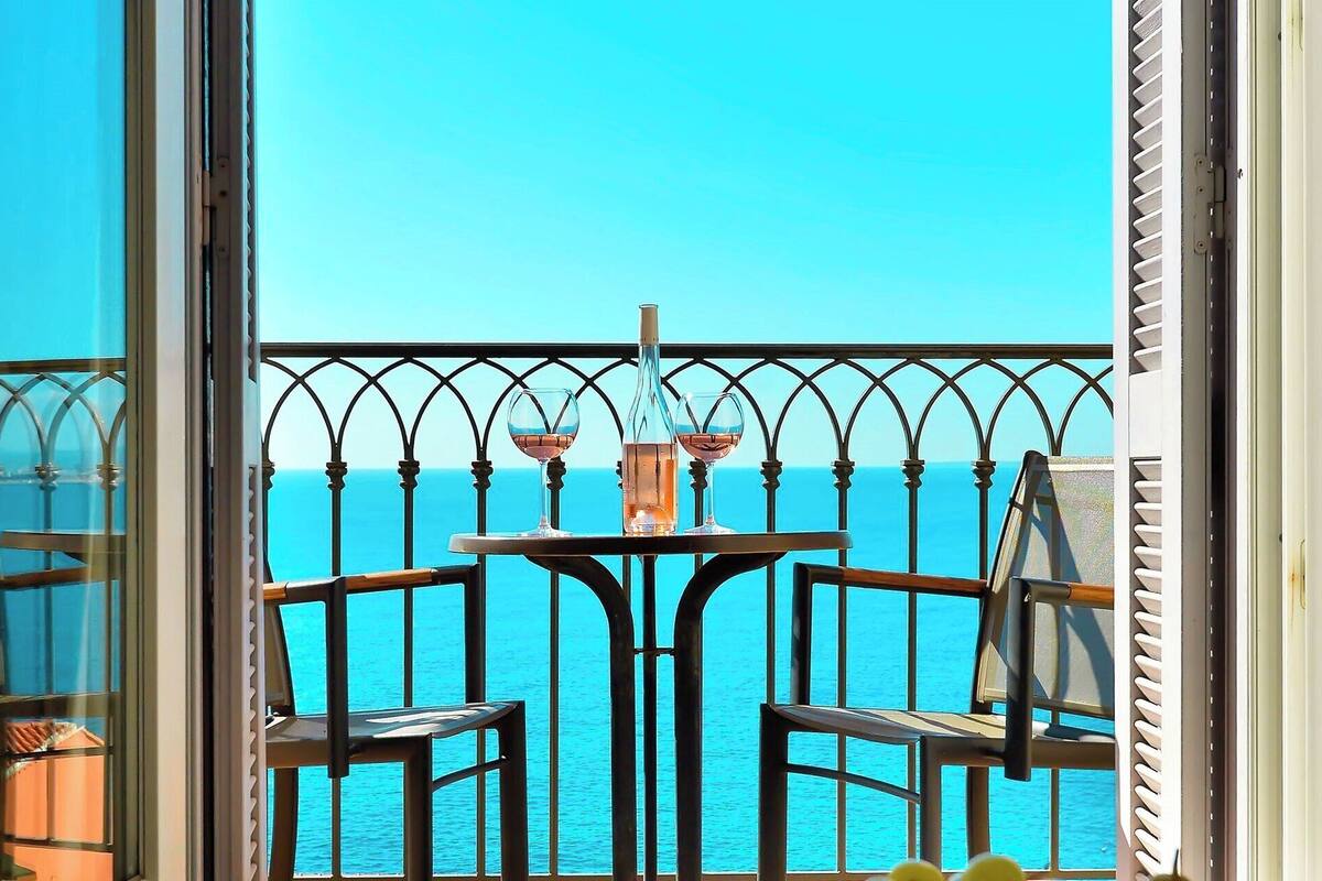 A balcony with a table and chairs, overlooking a clear blue sea.