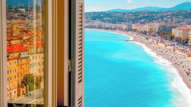 A balcony with a view of a coastal cityscape, featuring a beach and urban buildings. - Hôtel La Pérouse Nice (Nice)