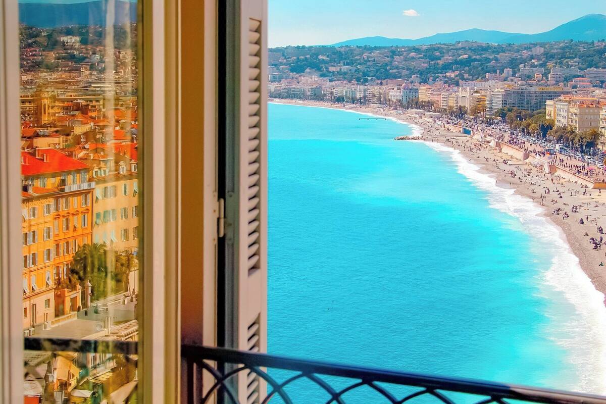 A balcony with a view of a coastal cityscape, featuring a beach and urban buildings.
