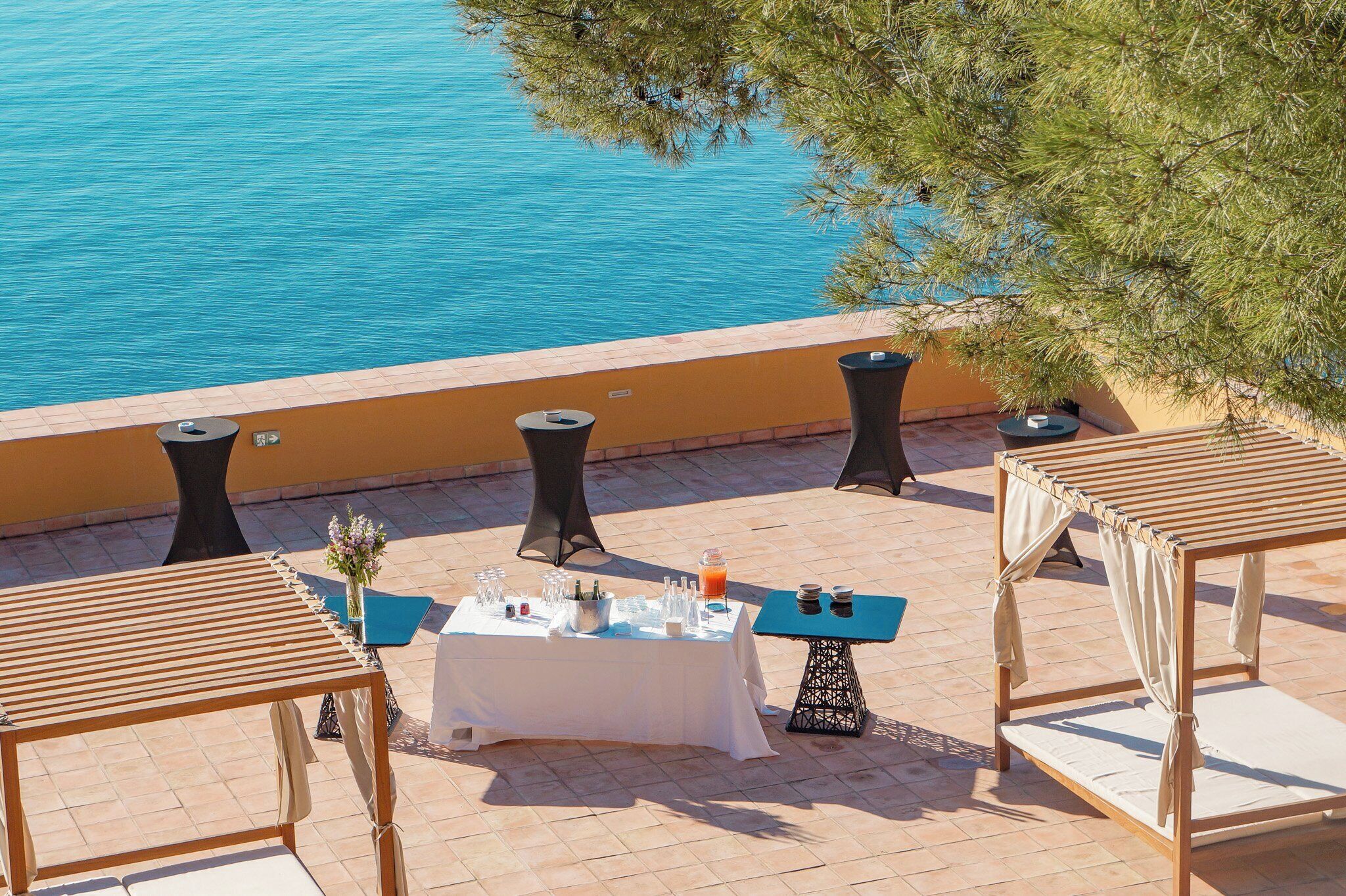 A terrace with a table set for a meal, overlooking a body of water.