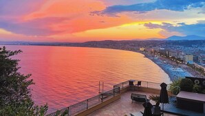 A seaside terrace with a view of the ocean and a cityscape during sunset. - Hôtel La Pérouse Nice (Nice)