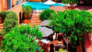 A hotel courtyard with a swimming pool, outdoor seating, and a view of a rocky cliff. - Hôtel La Pérouse Nice (Nice)