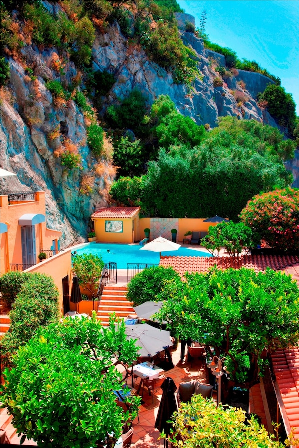 A hotel courtyard with a swimming pool, outdoor seating, and a view of a rocky cliff.