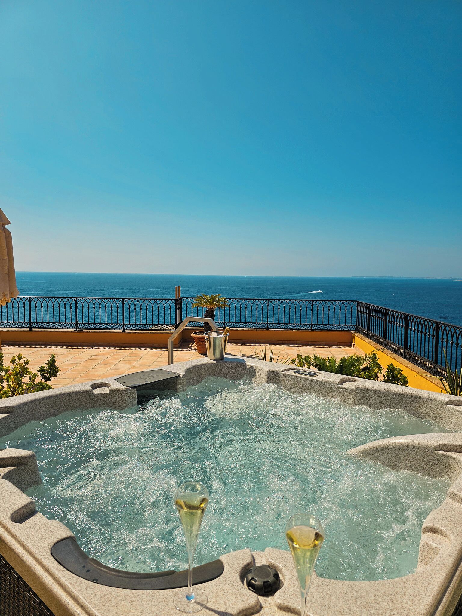 Ein Whirlpool mit zwei Sektgläsern, einer Palme und Blick auf das Meer.