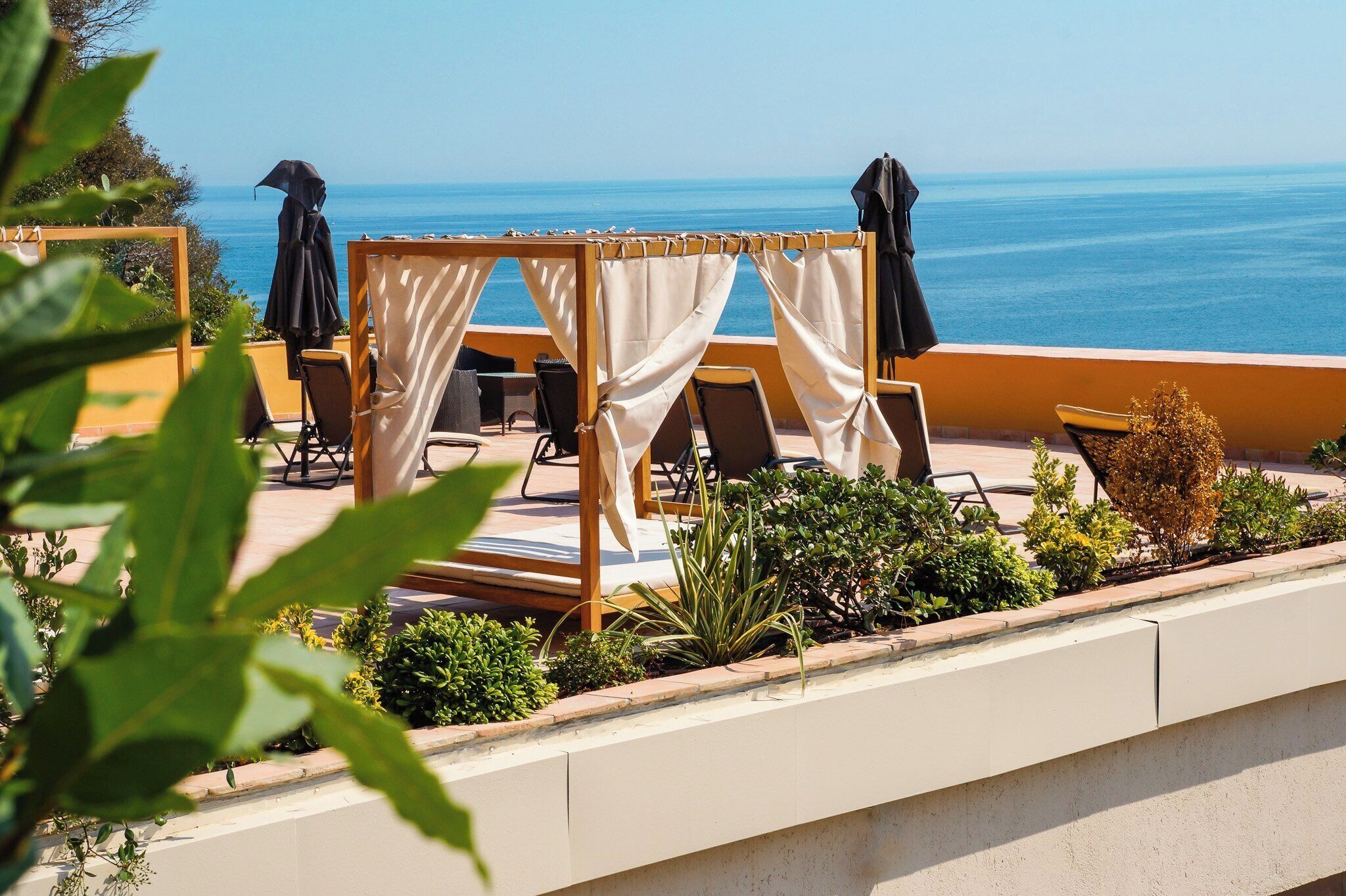 A sunlit outdoor seating area with a view of the sea, featuring a wooden chair and a small table.