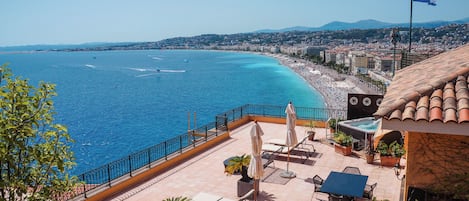 A rooftop terrace with outdoor seating, a pool, and a view of the coastline.