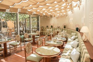 A restaurant with round tables and chairs, a curved sofa, and a large window overlooking greenery.