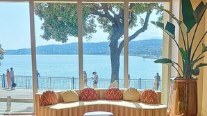 A curved sofa with patterned cushions, a small round table, and a large potted plant. - Hôtel La Pérouse Nice (Nice)