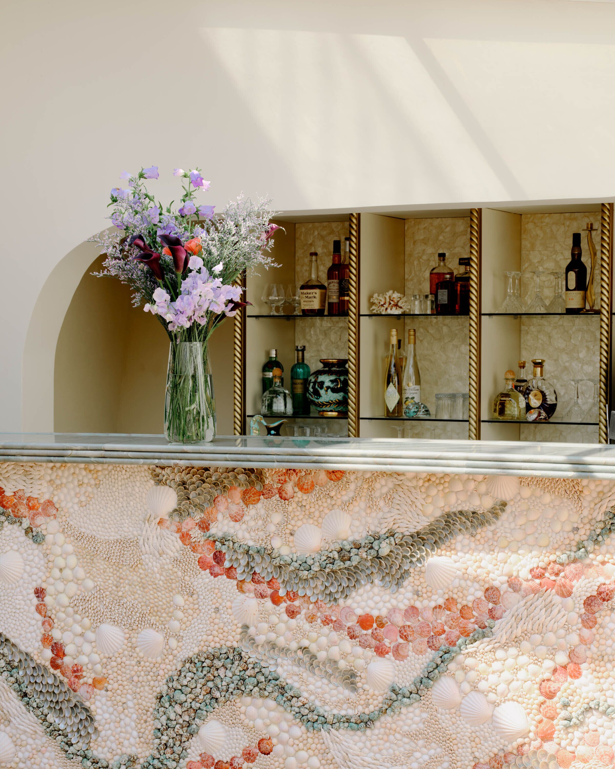A bar area with a floral arrangement, shelves of liquor bottles, and a decorative shell mosaic on the floor.