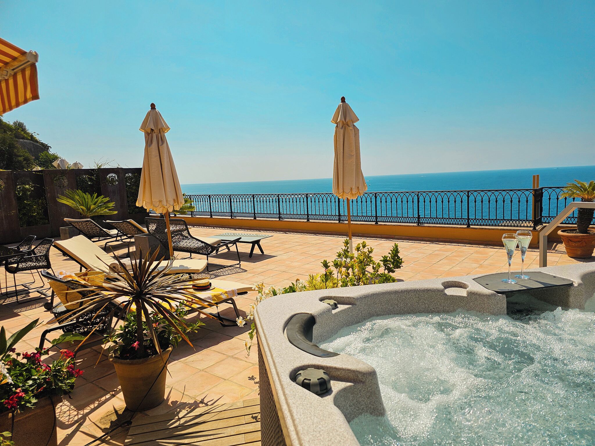 A rooftop terrace with lounge chairs, a hot tub, and a view of the sea.