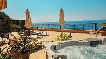A rooftop terrace with lounge chairs, a hot tub, and a view of the sea.