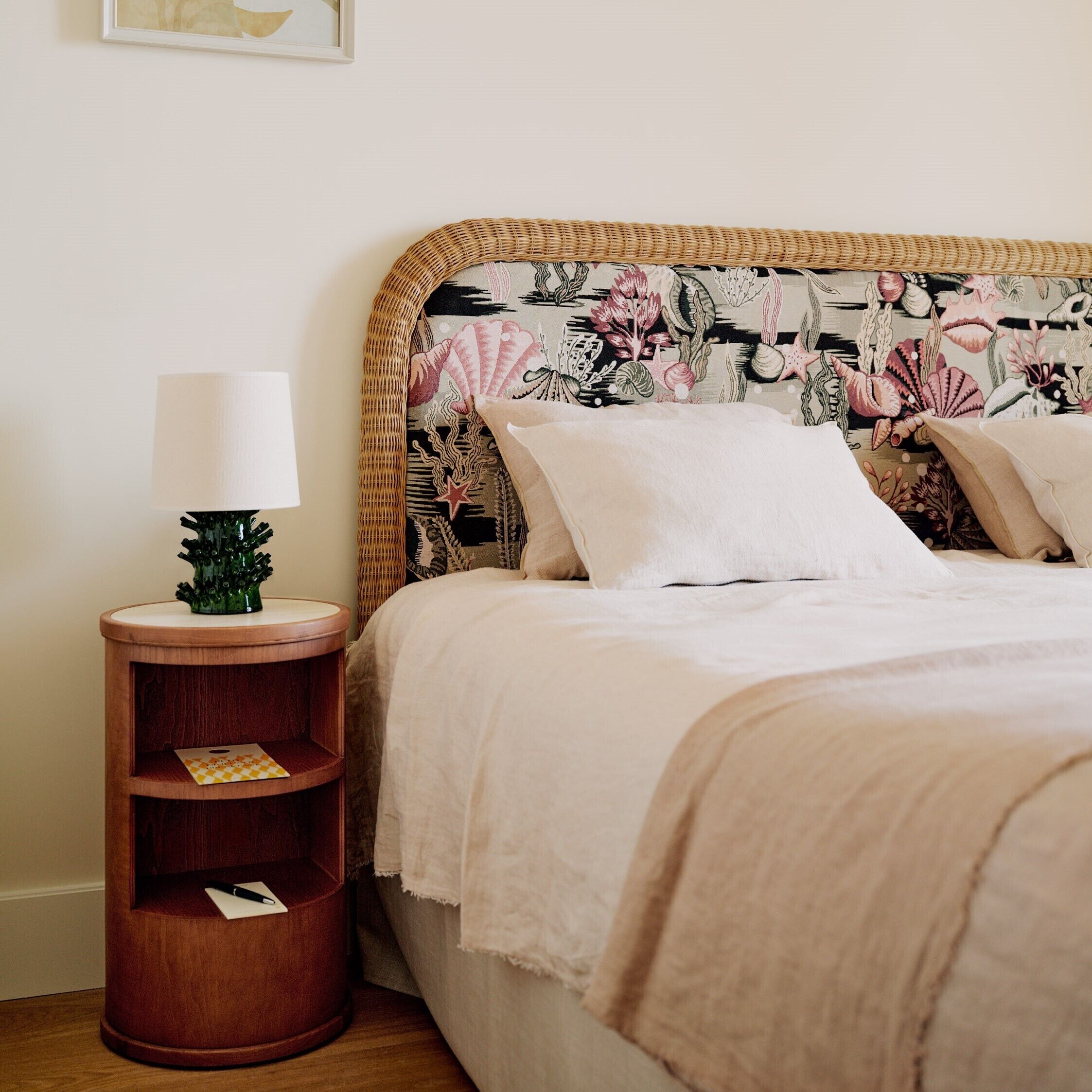 A bed with a floral headboard, a bedside table with a lamp, and a small green plant.