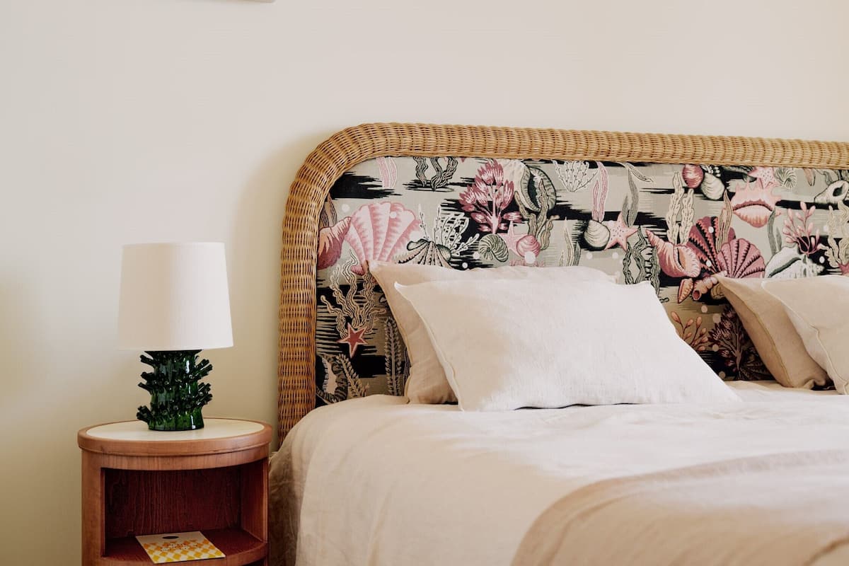 A bed with a floral headboard, a bedside table with a lamp, and a small green plant.