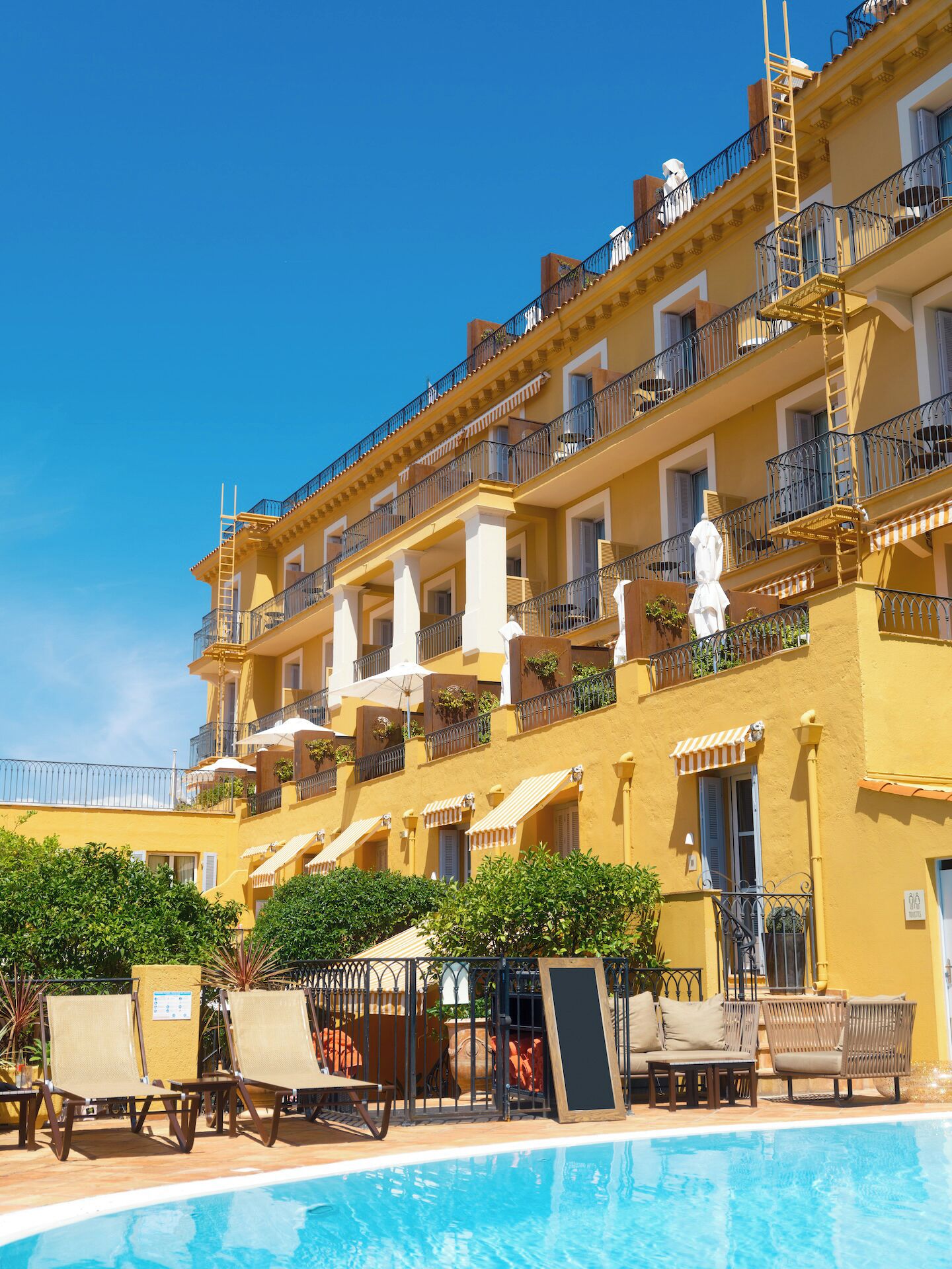 Um hotel com vários andares, varandas, piscina e área de estar ao ar livre.