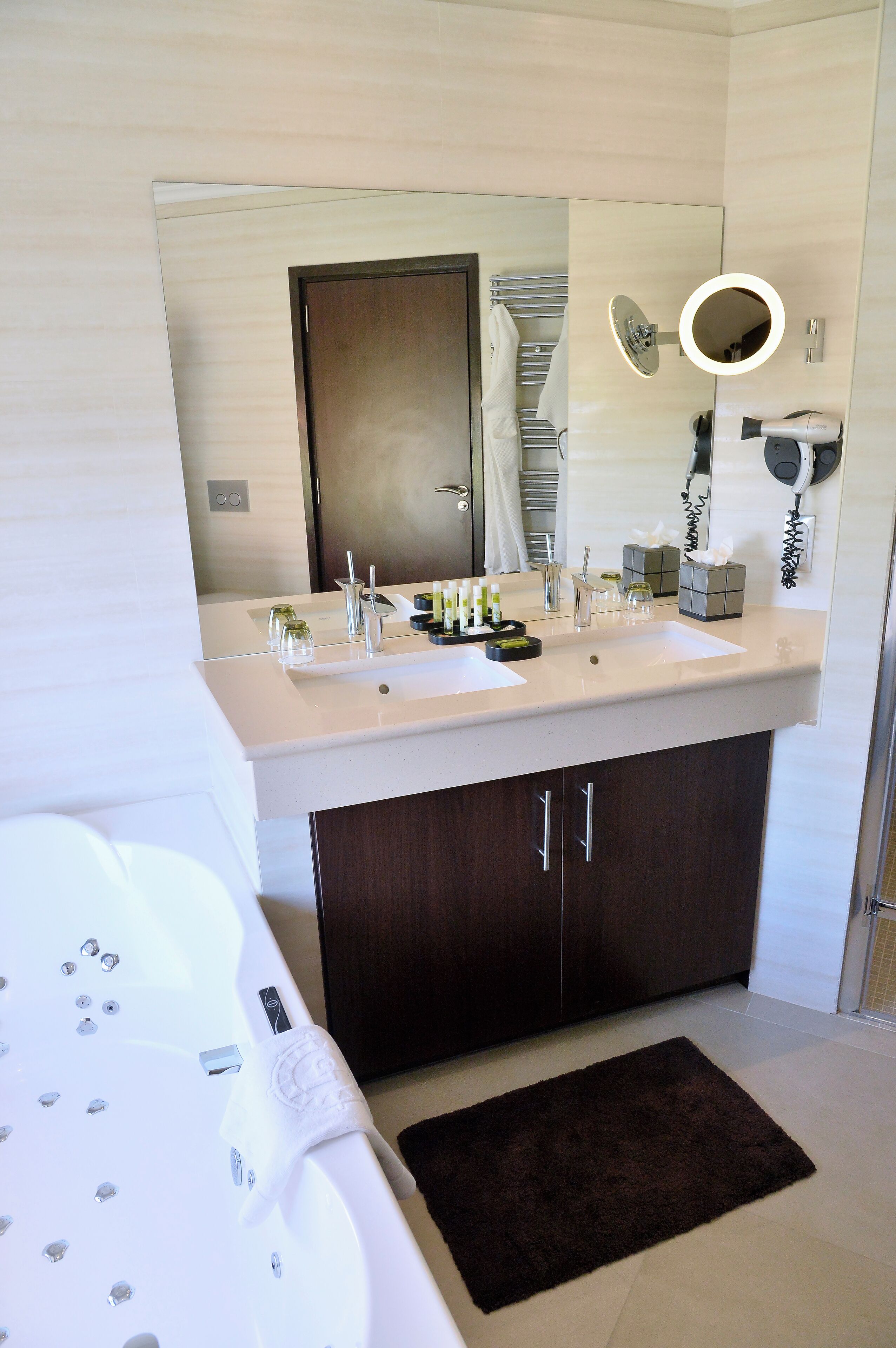 A modern bathroom with a double sink, a large mirror, a hairdryer, and a towel rack.