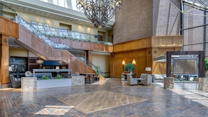 A spacious lobby with a wooden floor, a staircase, and a glass railing.