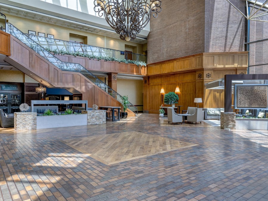 A spacious lobby with a wooden floor, a staircase, and a glass railing.