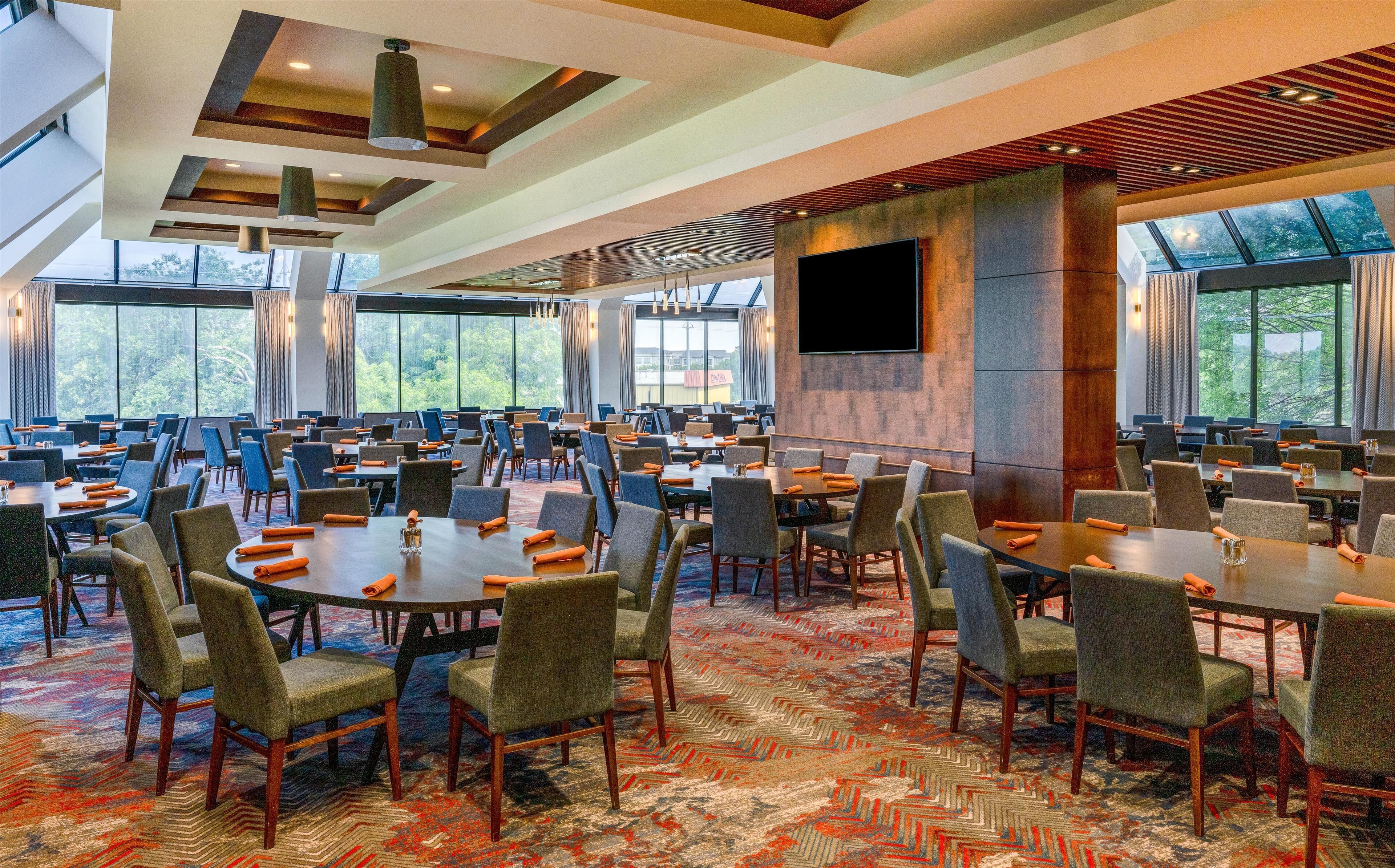 A large conference room with multiple tables and chairs, large windows, and a modern ceiling design.