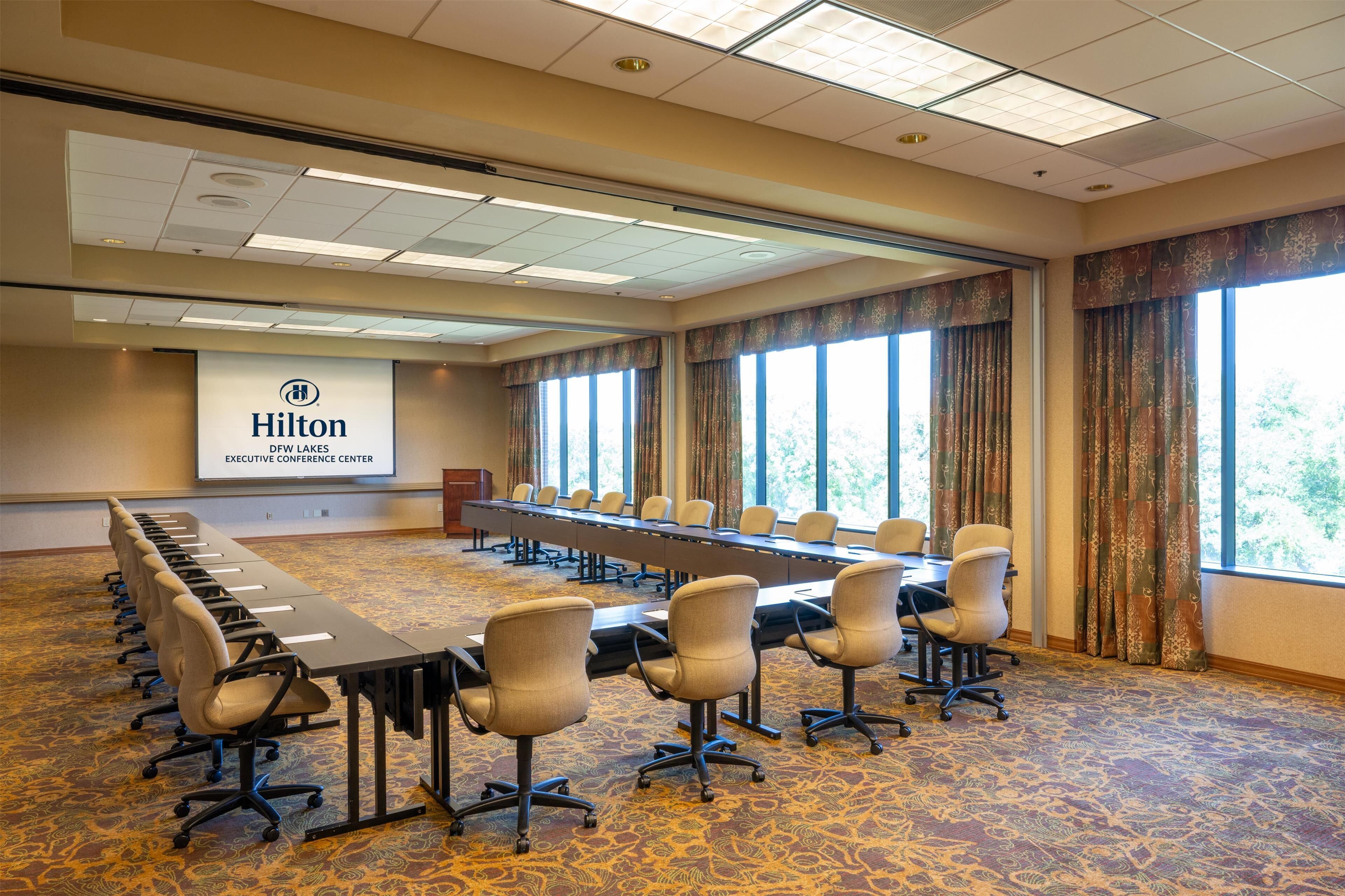 A conference room with a long table, chairs, and a projector screen displaying the Hilton logo.