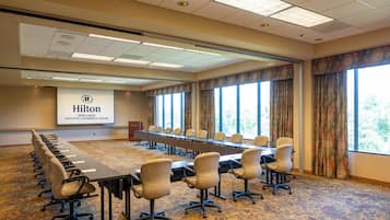 A conference room with a long table, chairs, and a projector screen displaying the Hilton logo.