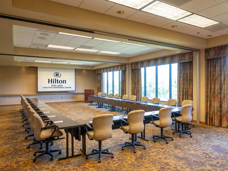 A conference room with a long table, chairs, and a projector screen displaying the Hilton logo.
