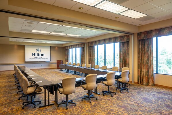 Un salón de conferencias con una larga mesa, sillas y una pantalla proyectora mostrando el logotipo de Hilton.