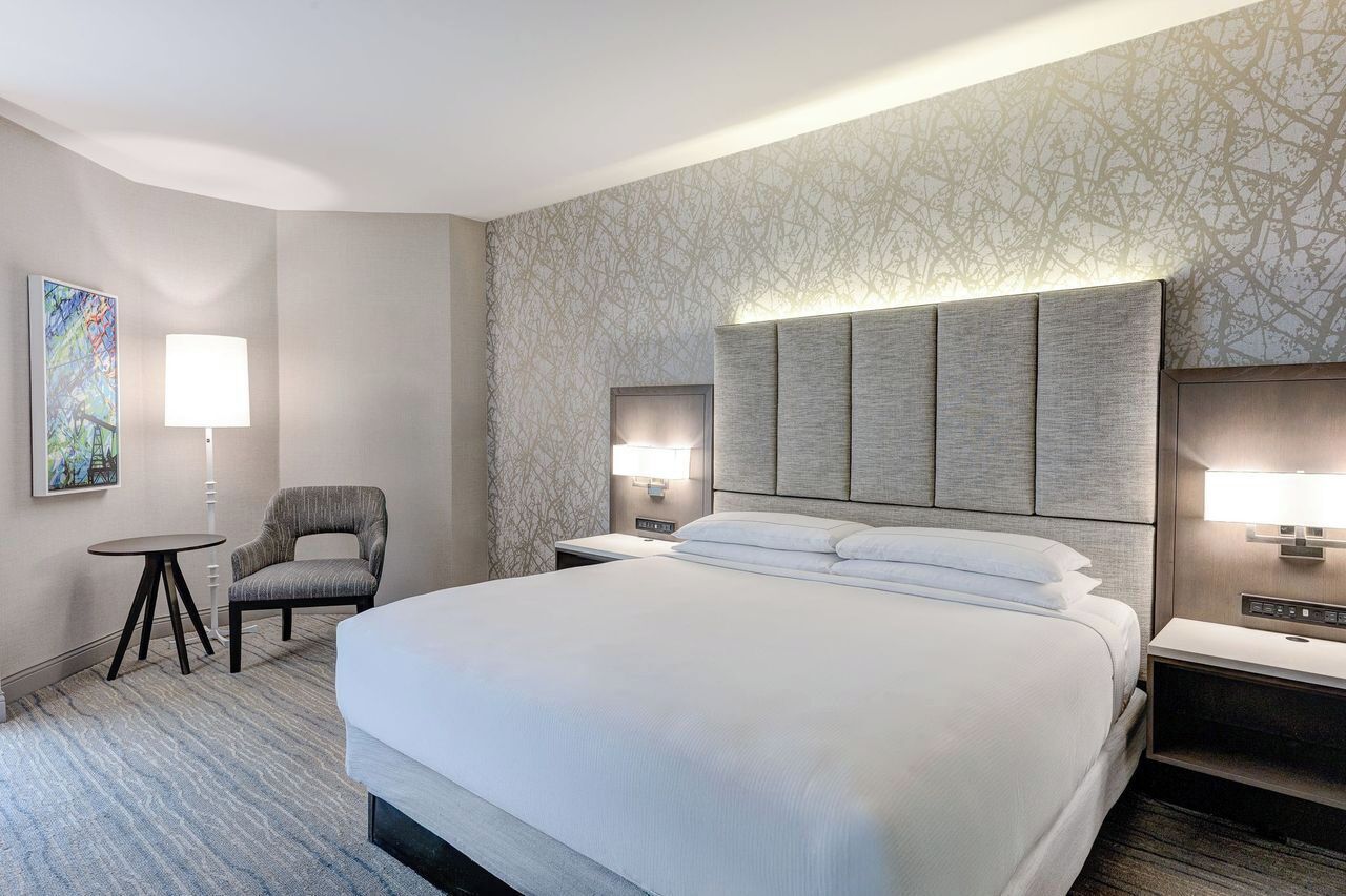 Habitación de hotel con una cama grande, una silla, una mesita y dos lámparas de noche.