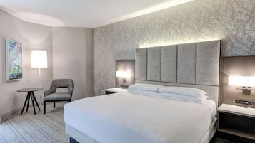 Habitación de hotel con una cama grande, una silla, una mesita y dos lámparas de noche.
