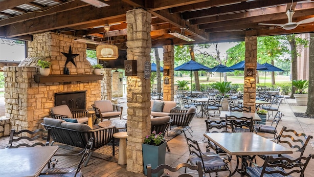 An outdoor patio area with stone walls, wooden beams, and various seating arrangements including tables and chairs.