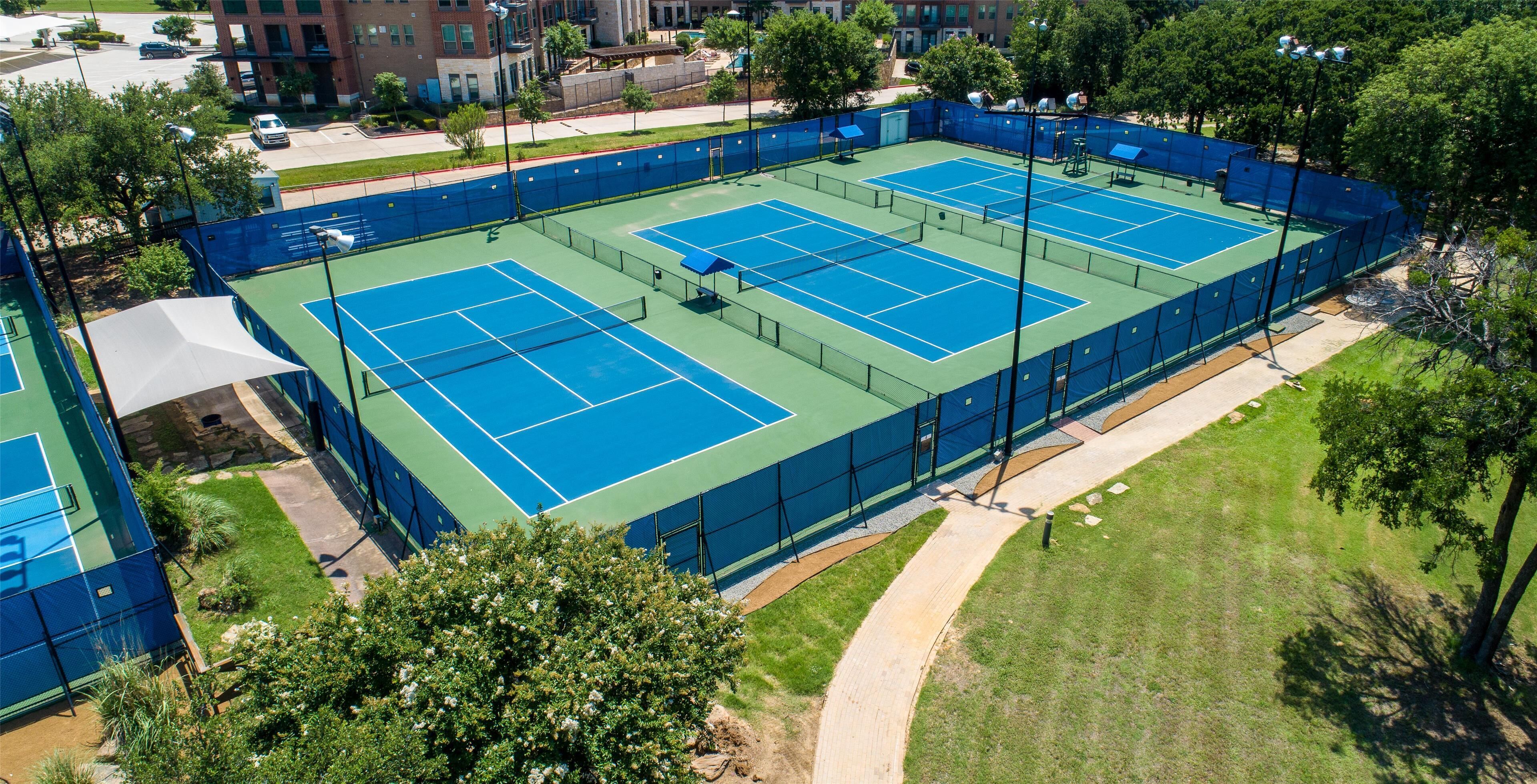An outdoor tennis court surrounded by trees and buildings.
