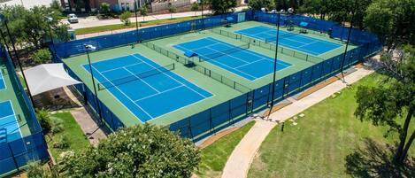 An outdoor tennis court surrounded by trees and buildings.