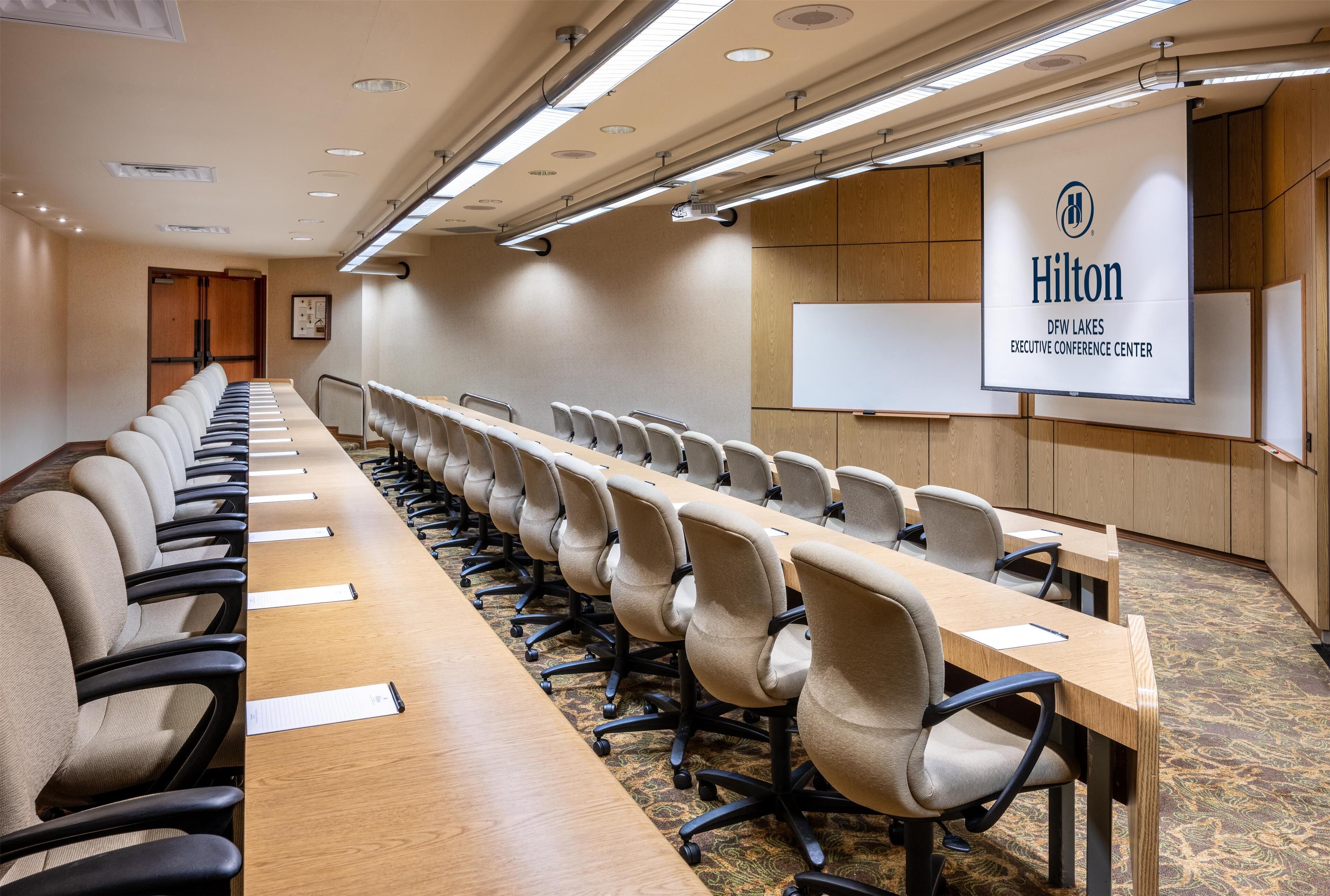 A conference room with a long table, chairs, a whiteboard, and a sign indicating it's the Hilton Executive Conference Center.