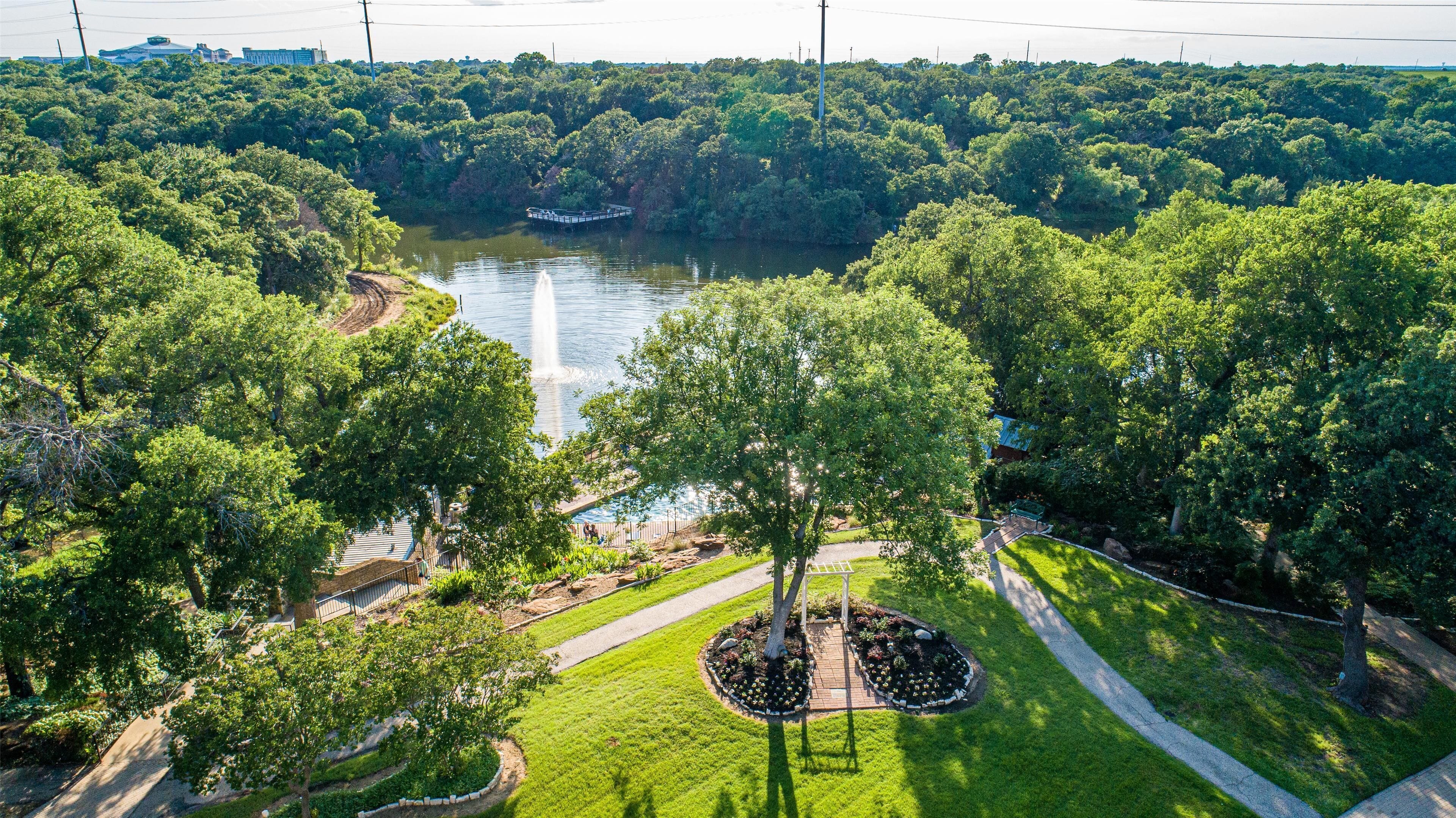 An aerial view of a park with a river, walking paths, and a central circular garden.