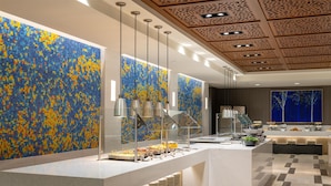 A modern hotel lobby with a large mosaic wall, a buffet area, and a seating area.