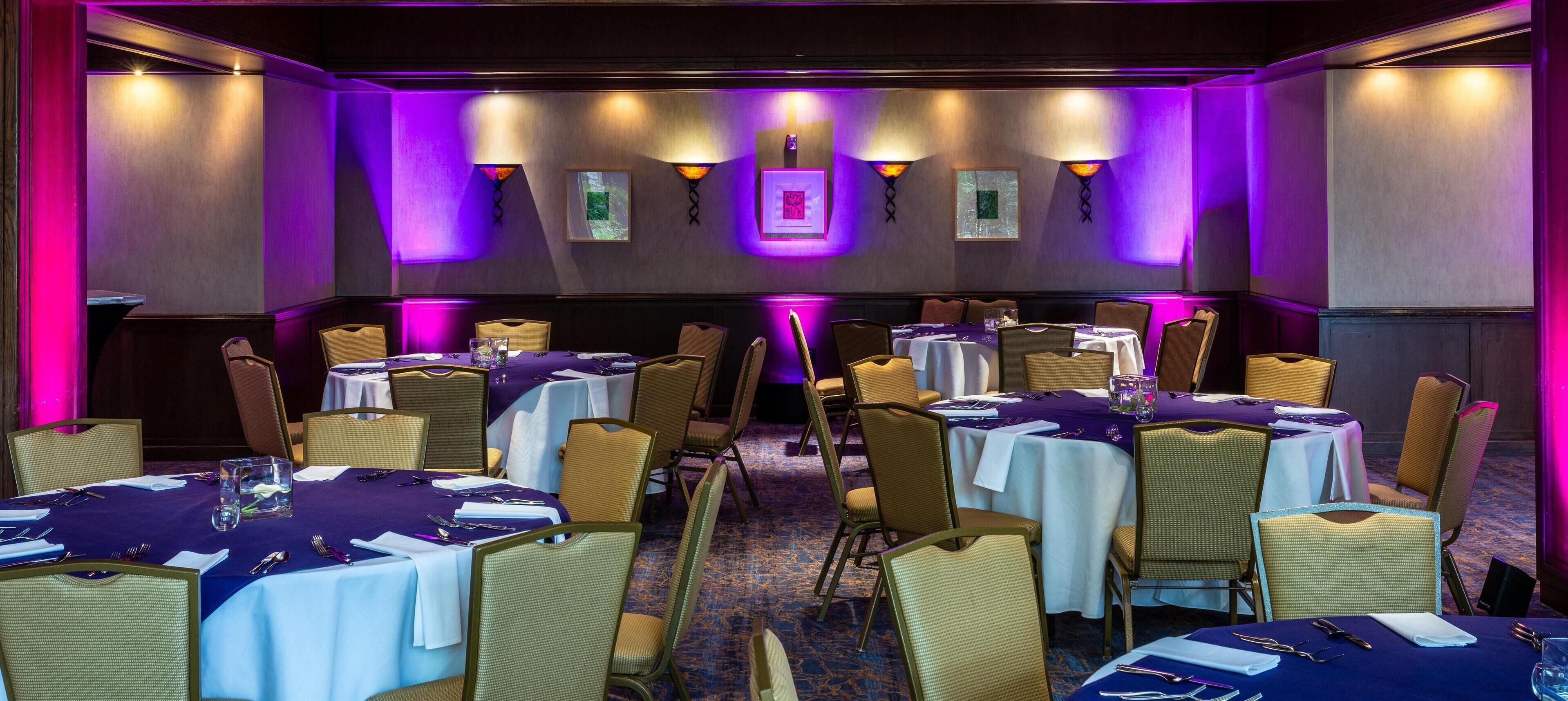 A conference room with multiple tables and chairs, purple ambient lighting, and framed pictures on the walls.