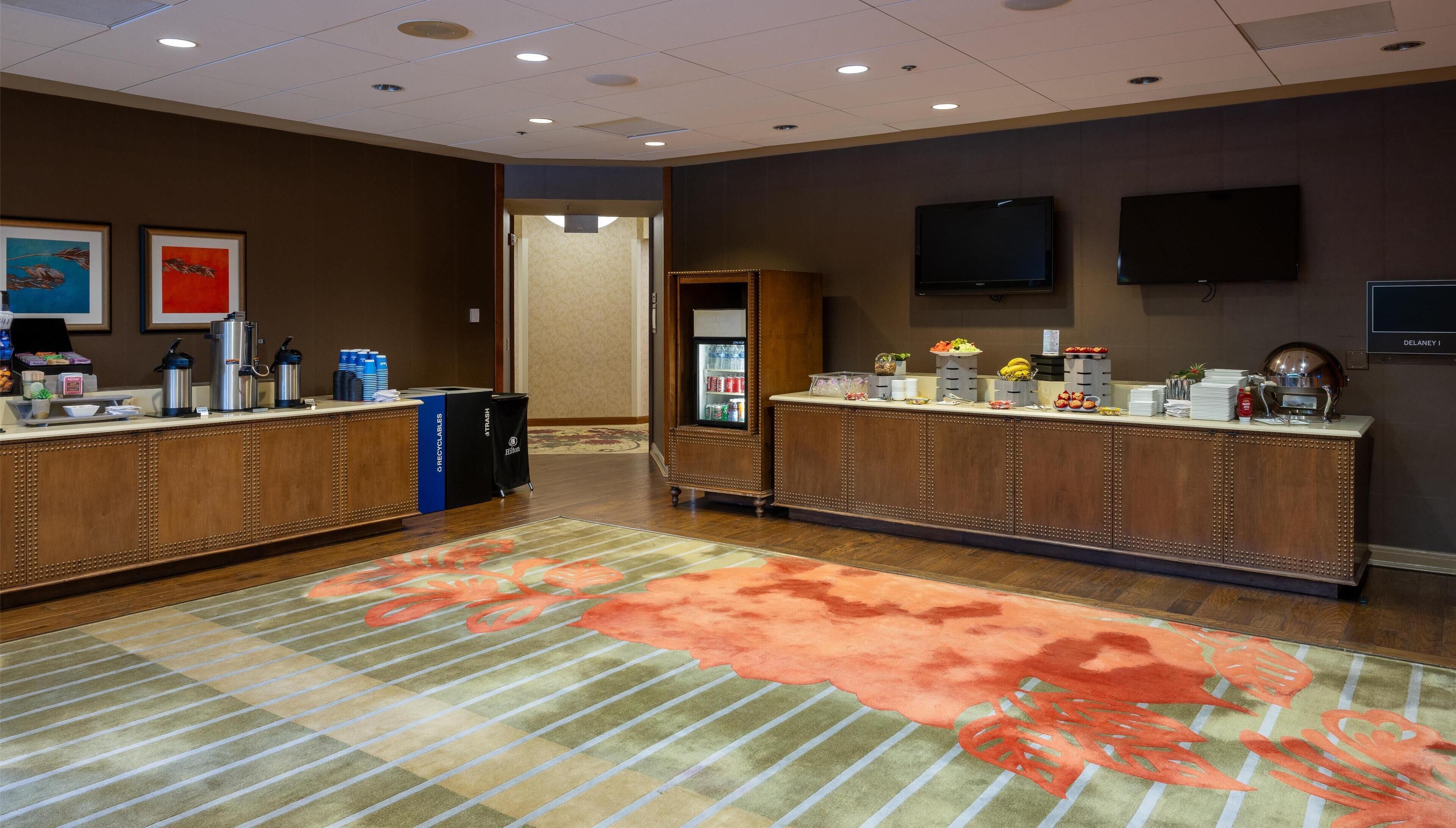 A hotel reception area with two reception desks, a refrigerator, and a flat-screen TV on the wall.