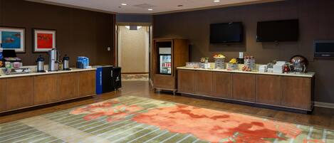 A hotel reception area with two reception desks, a refrigerator, and a flat-screen TV on the wall.