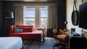 Ein Hotelzimmer mit einem roten Sofa, einem Holztisch, einem Stuhl, einem Bett und einem großen Fenster zur Stadt.