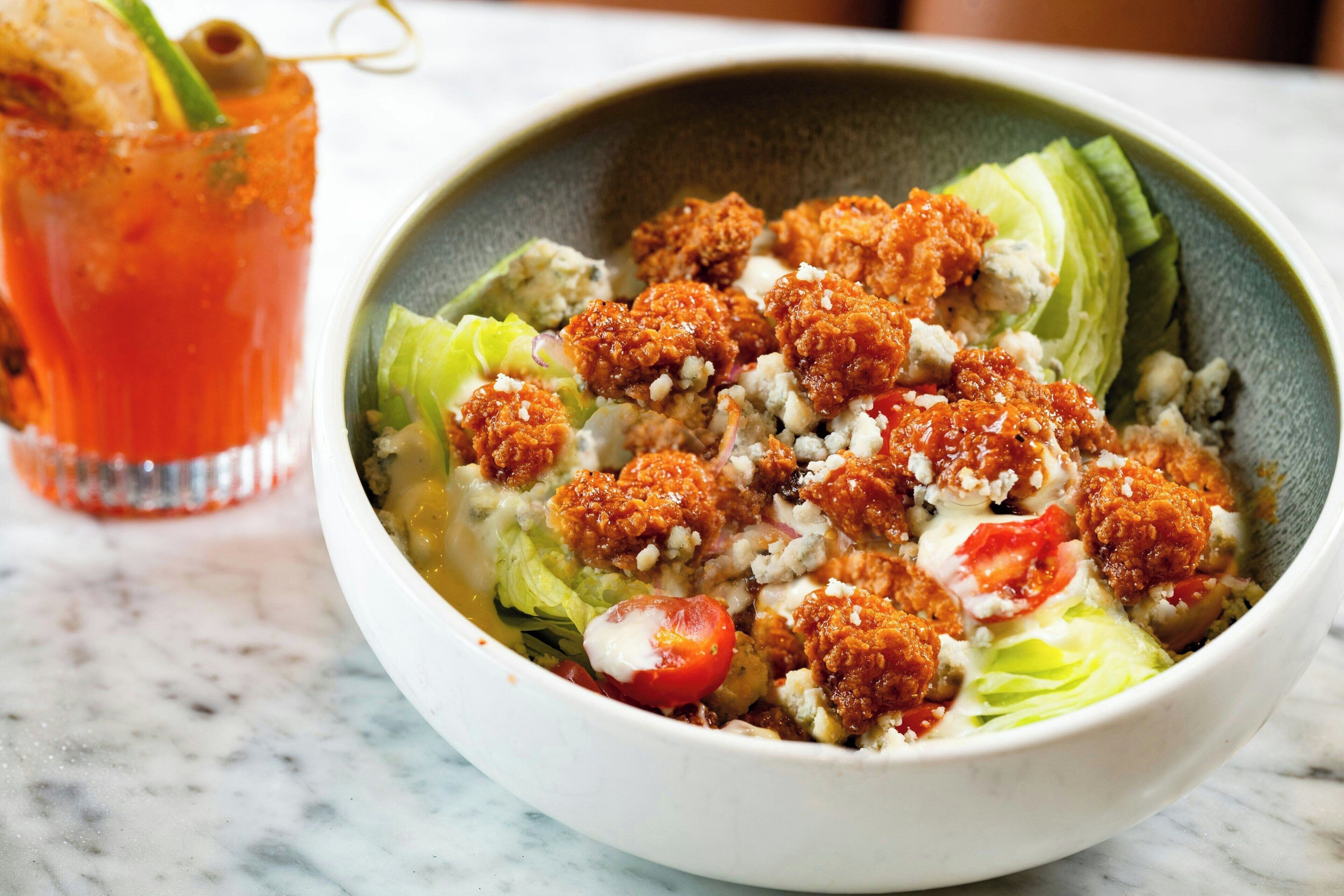 A bowl of salad with crumbled cheese and a glass of red drink.
