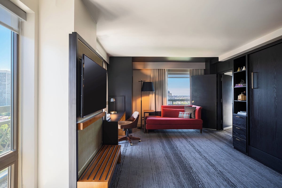 Une chambre d’hôtel moderne équipée d’une grande télévision, d’un canapé rouge, d’un bureau avec une chaise et d’une bibliothèque.