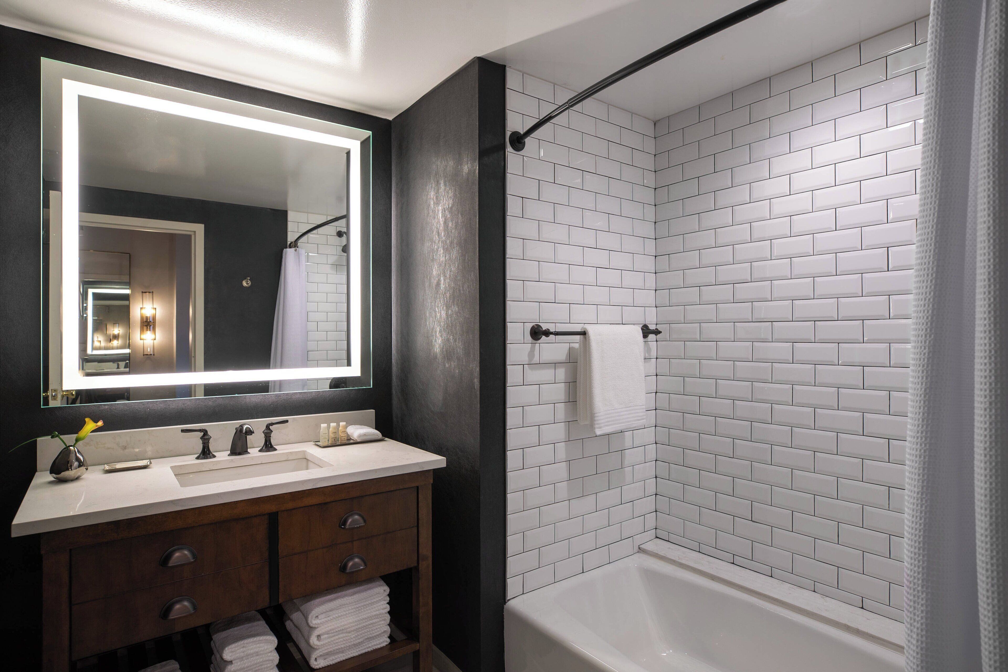 A modern bathroom with a white-tiled shower, a large mirror, and a vanity with a dark wood finish.