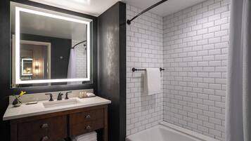 A modern bathroom with a white-tiled shower, a large mirror, and a vanity with a dark wood finish.