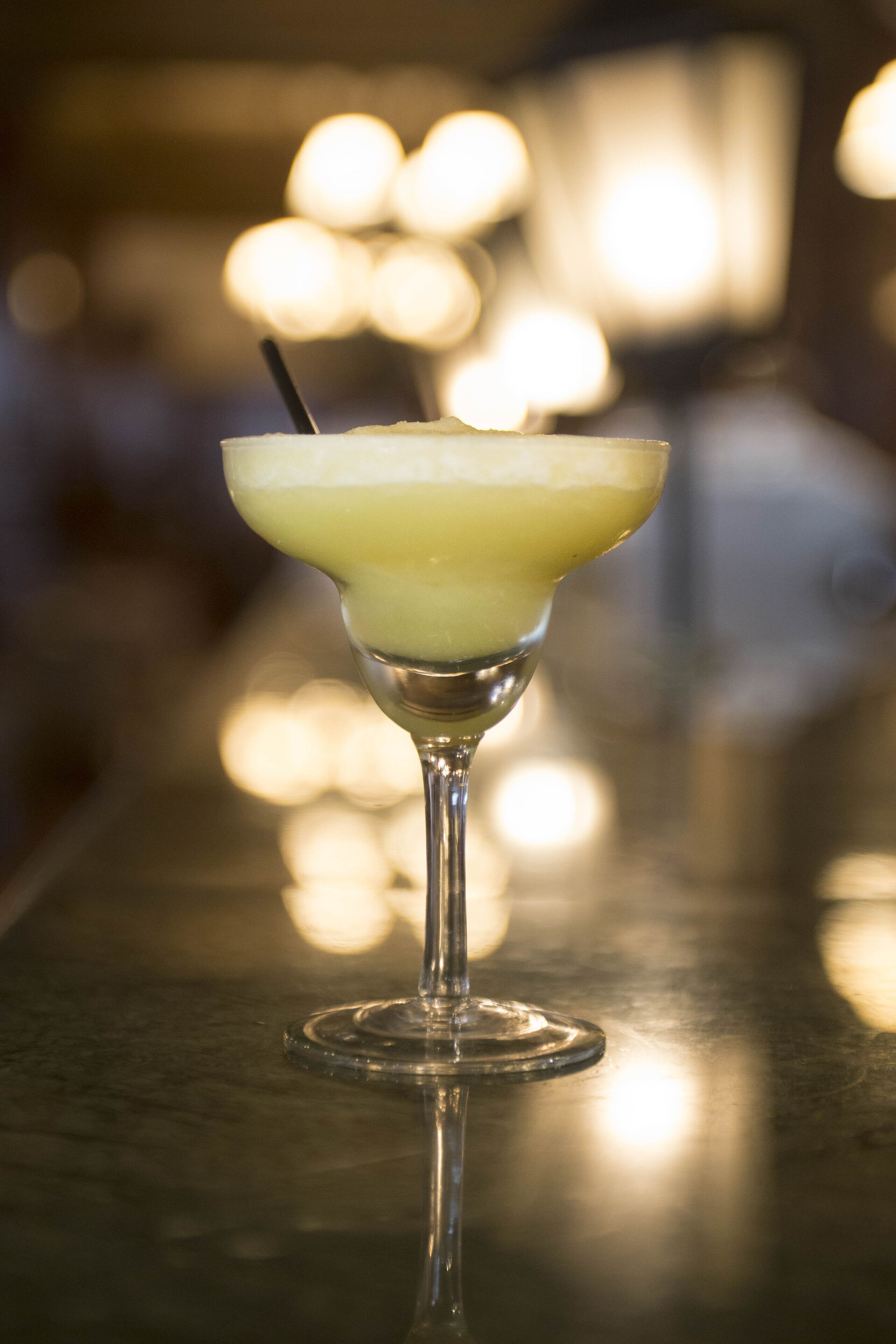 Un cóctel en una copa de martini con pajita sobre una barra.