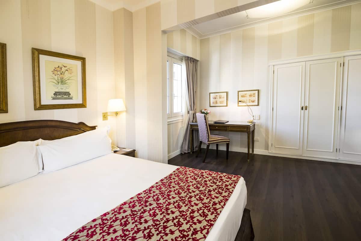 A hotel room with a large bed, a desk, and a wardrobe.
