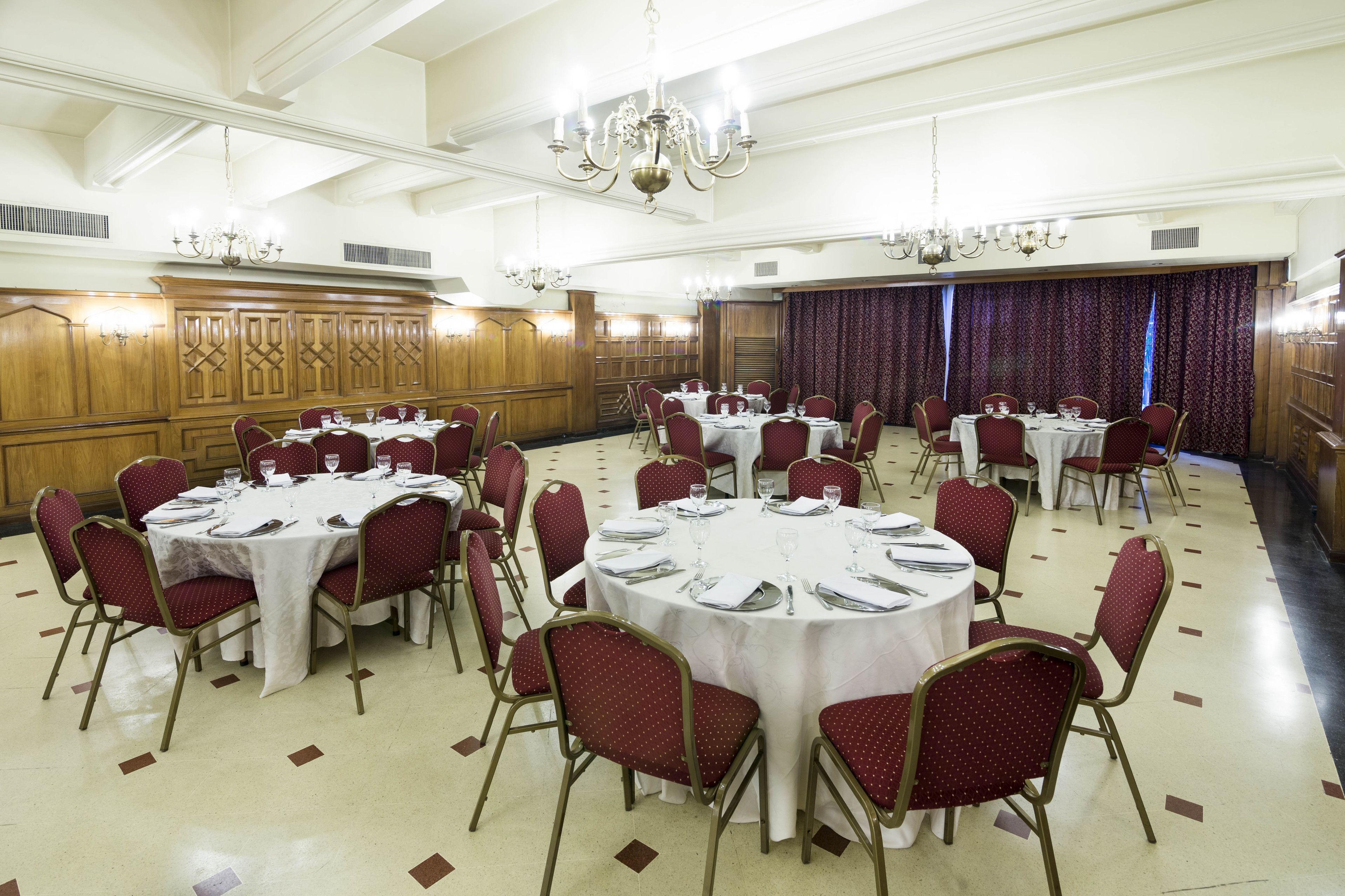 Un salón de banquetes con mesas redondas y sillas tapizadas en rojo, paneles de madera en las paredes y candelabros.