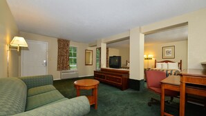 A hotel room with a green sofa, a wooden desk, a television, and a bed with a headboard.
