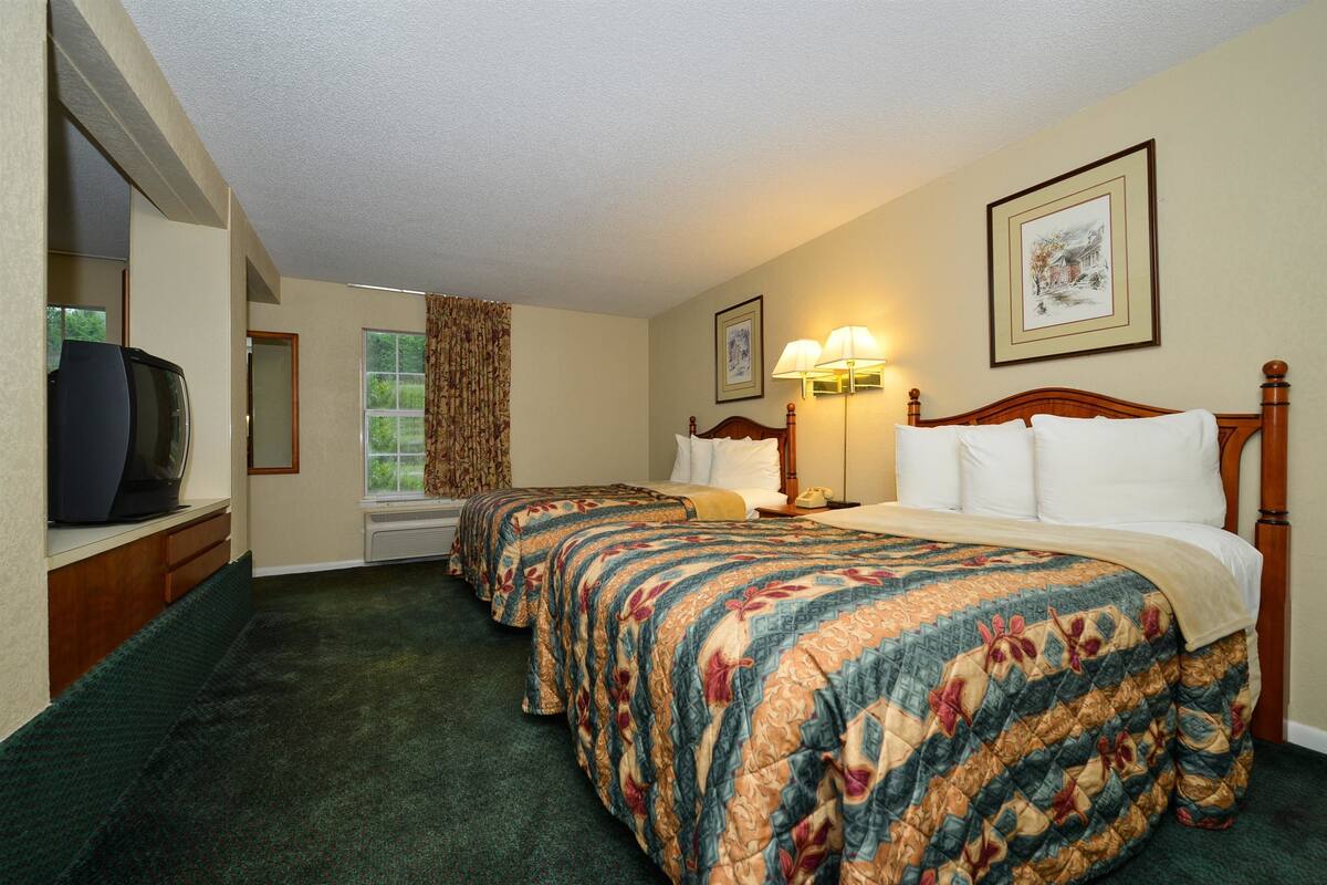 A hotel room with two beds, a television, a window with curtains, and a framed picture on the wall.