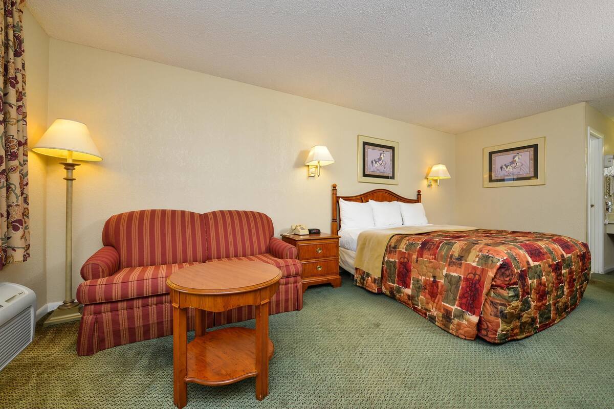 A hotel room with a single bed, a sofa, a small table, and two wall-mounted lamps.