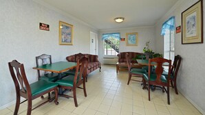Un espace repas avec des tables et des chaises en bois, un canapé et des œuvres d’art encadrées accrochées aux murs.