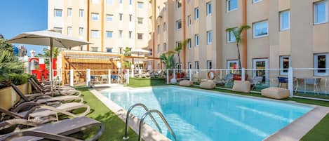 Una piscina al aire libre, sombrillas, sillones reclinables de piscina